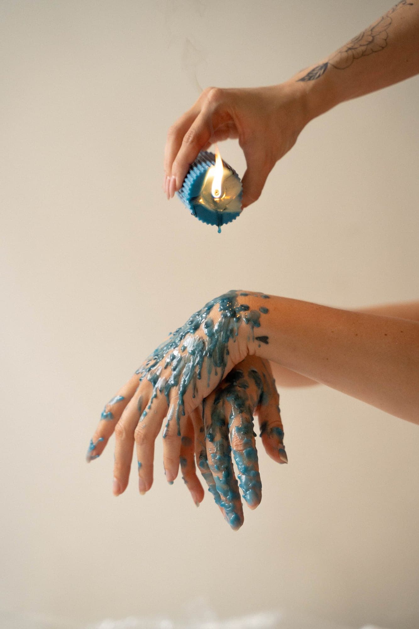 Teal wax dripping from a lit candle over the back of a hand